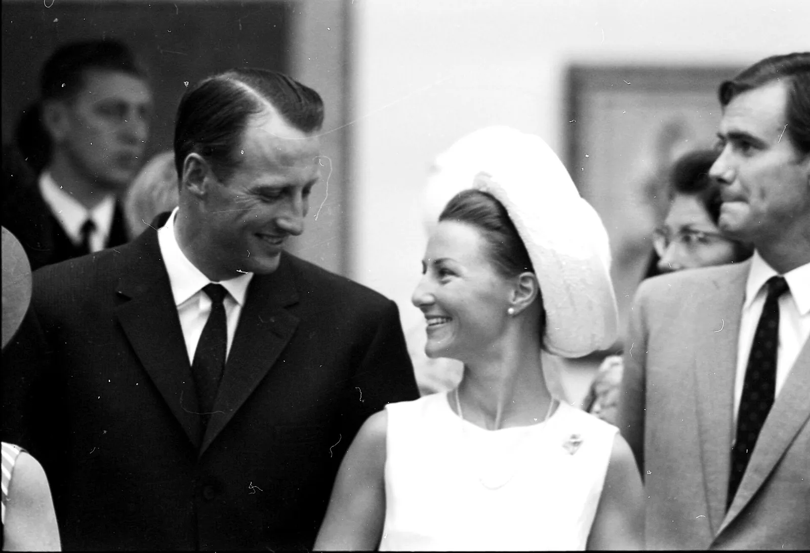 Kronprins Harald og Sonja Haraldsen ser på hverandre og ler, omgitt av folk. Svart-hvitt-bilde fra 1968.